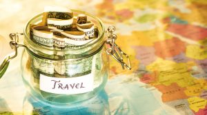 A jar with dollar bills in it on a map that reads "travel"