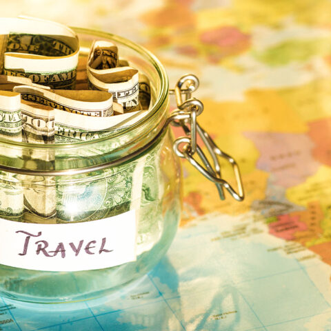 A jar with dollar bills in it on a map that reads "travel"