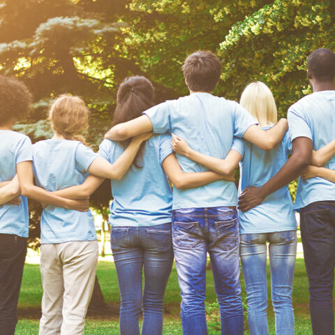 A group of people in blue shirts with their backs facing us and arms wrapped around each other