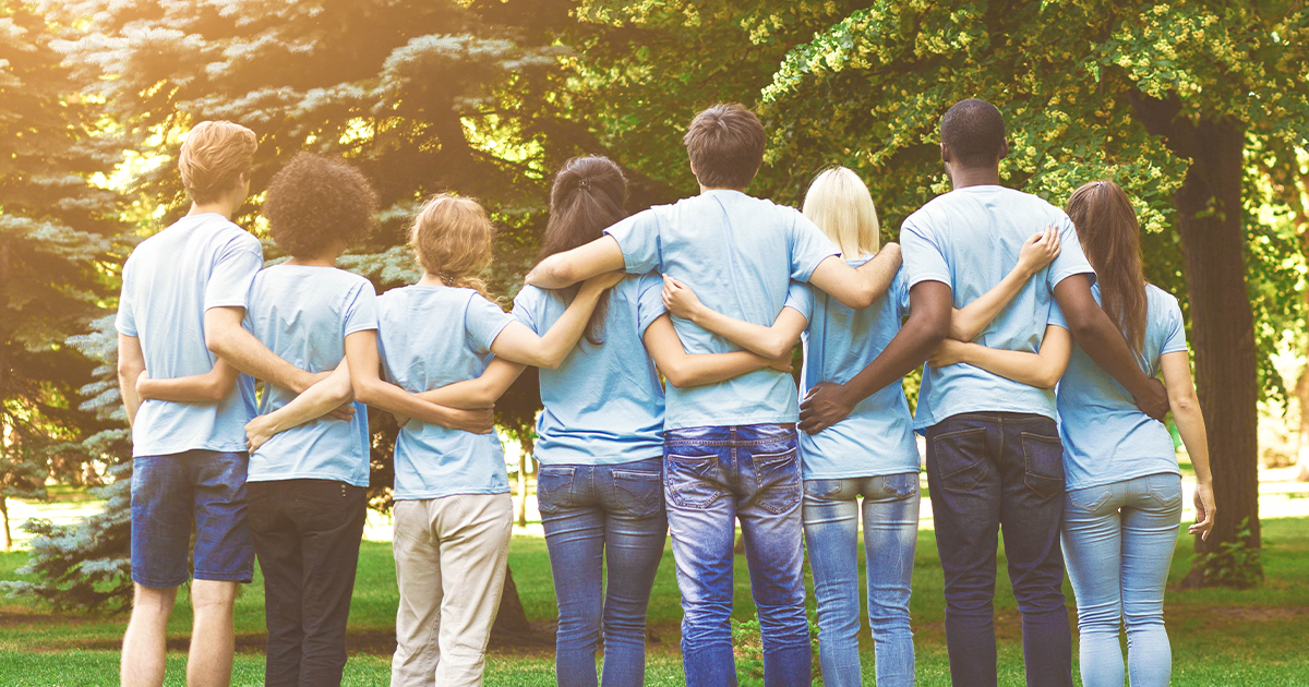 A group of people in blue shirts with their backs facing us and arms wrapped around each other