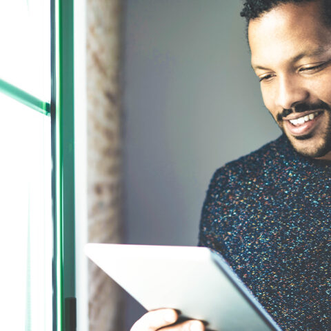 Man in a grey sweater using an IPAD by a green window