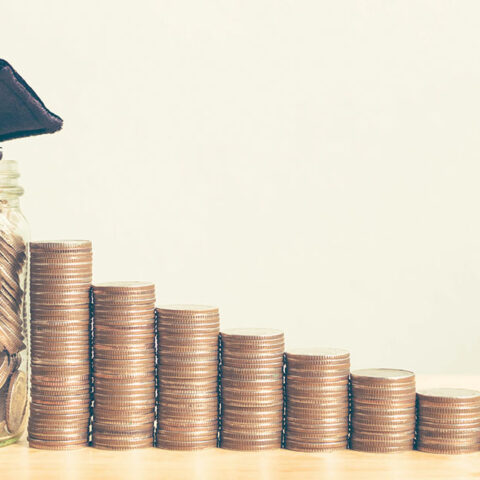 Stacked quarters next to a mason jar filled with coins and a graduation cap on top.