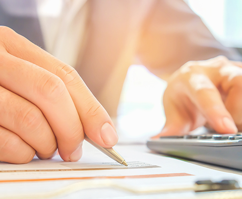 hands writing and typing into a calculator preparing taxes