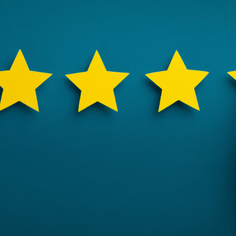 Hand arranging five gold stars on a dark background.